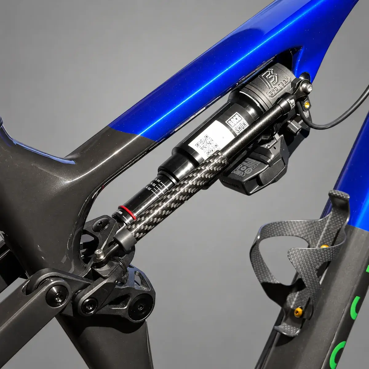 A blue Rockrider Race 940 S with a linear sensor running diagonally from the printed link bracket alongside the rear shock, against a grey background.