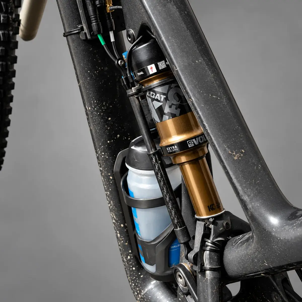 A Specialized Stumpjumper Evo with a linear sensor fitted alongside the Fox Float rear shock and a bottle behind it, against a grey background.