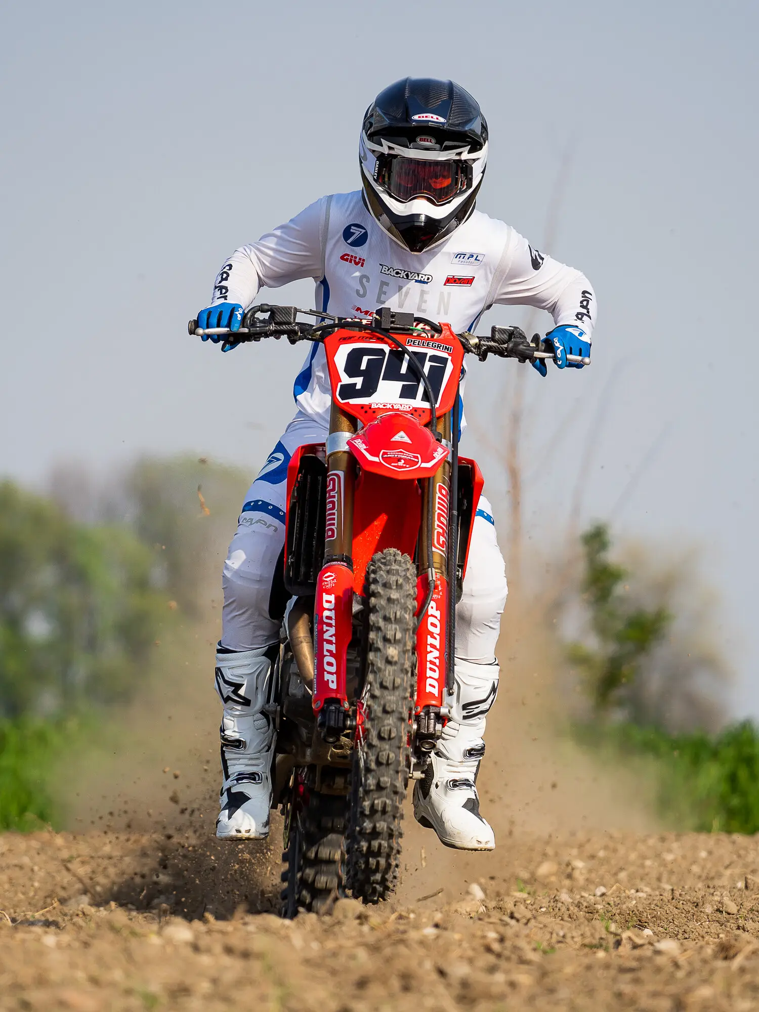 A motocross rider landing on a dirt track, front wheel down and dust thrown up behind the bike.