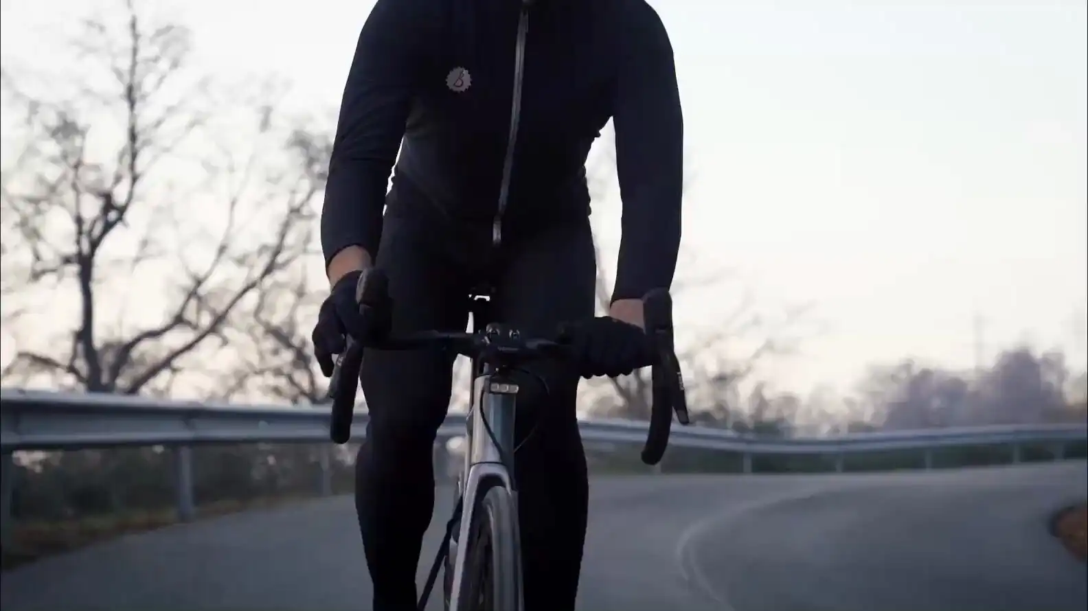 A road cyclist riding towards the camera at dusk on an empty road, a BYB Focus mounted beneath the handlebar.