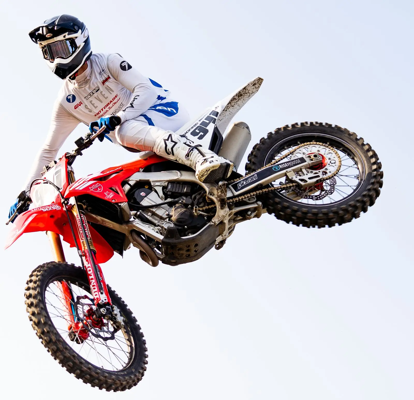 A red Honda motocross bike airborne side-on against a clear sky, with a BYB Telemetry linear sensor running down the fork leg and the acquisition unit mounted on the front number plate.
