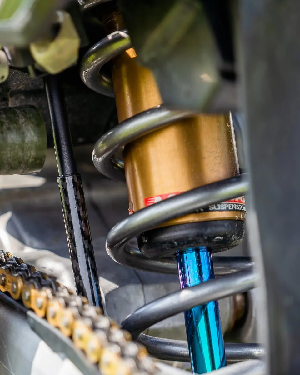 A BYB Telemetry linear sensor mounted alongside the coil shock of a motocross bike, its carbon-covered body running parallel to the spring.