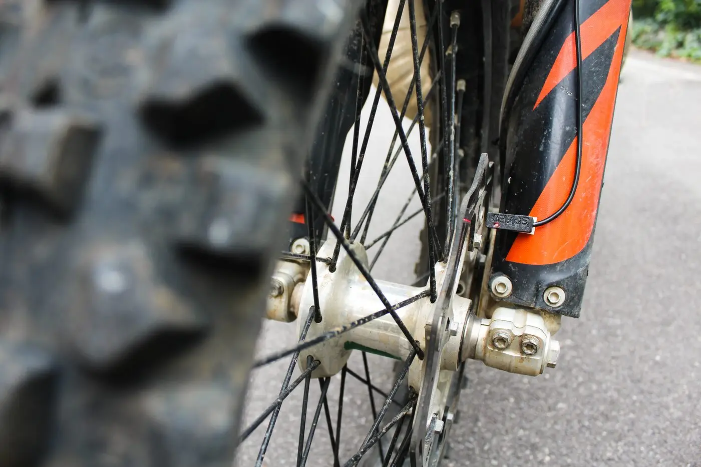 A BYB Telemetry speed sensor marked SPEED, mounted to the fork guard of a KTM on a bracket reaching in toward the front wheel spokes.
