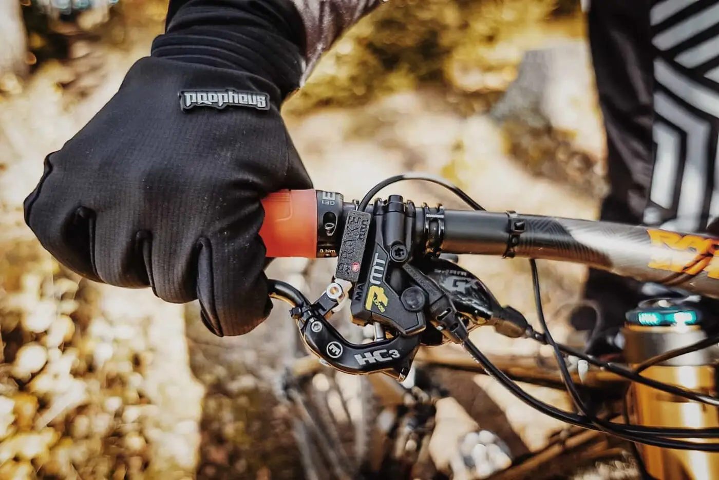 A BYB Telemetry brake sensor fitted at the lever on a mountain bike handlebar, with a gloved hand on the grip and the hydraulic hose unbroken.