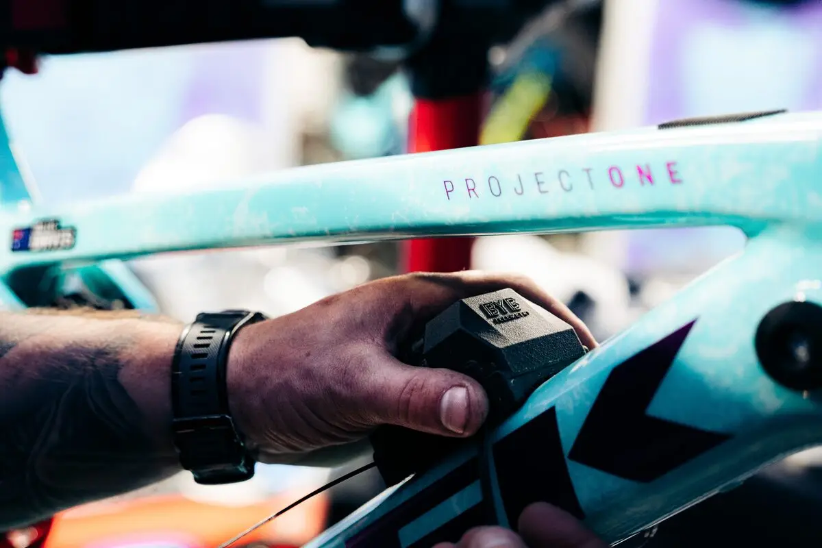 A mechanic's hands fitting a BYB Telemetry acquisition unit to the down tube of a downhill mountain bike.