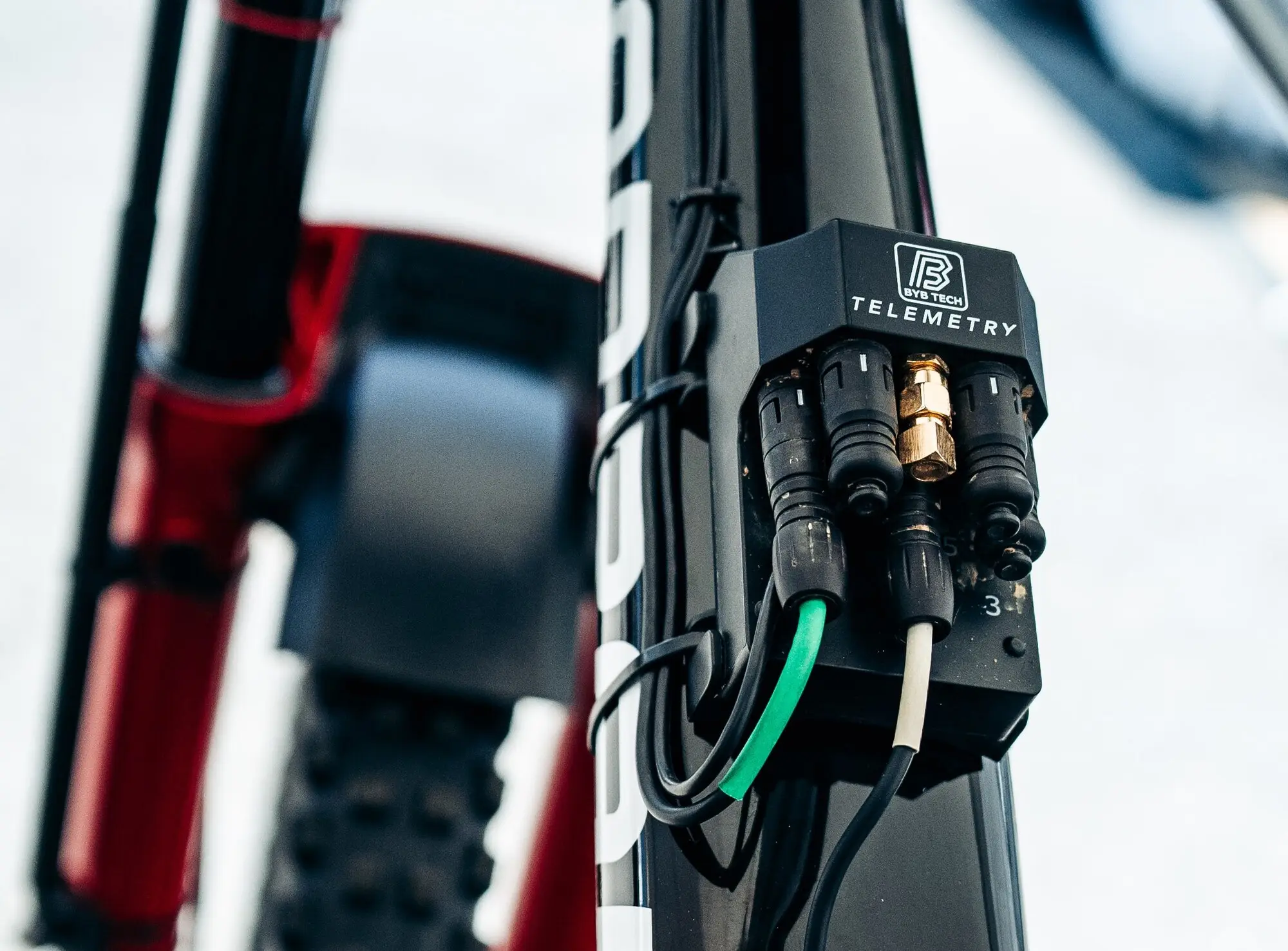 A BYB Telemetry V3 Pro acquisition unit strapped to the frame of a downhill mountain bike, sensor cables plugged into the connectors on its face with a gold GPS antenna fitting among them.
