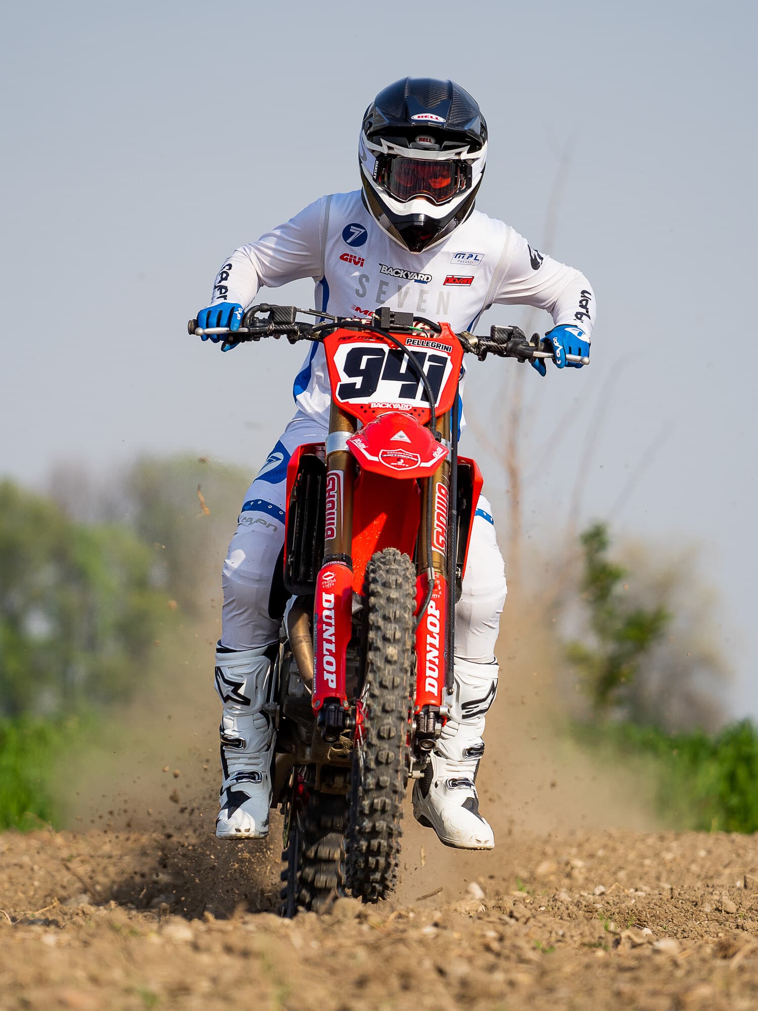 A motocross rider landing on a dirt track, front wheel down and dust thrown up behind the bike.