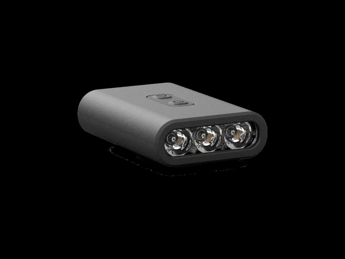 The BYB Focus bike light at three-quarters, unlit: a wide low body in dark grey with three lenses set in a row across the front and two buttons on the top face.