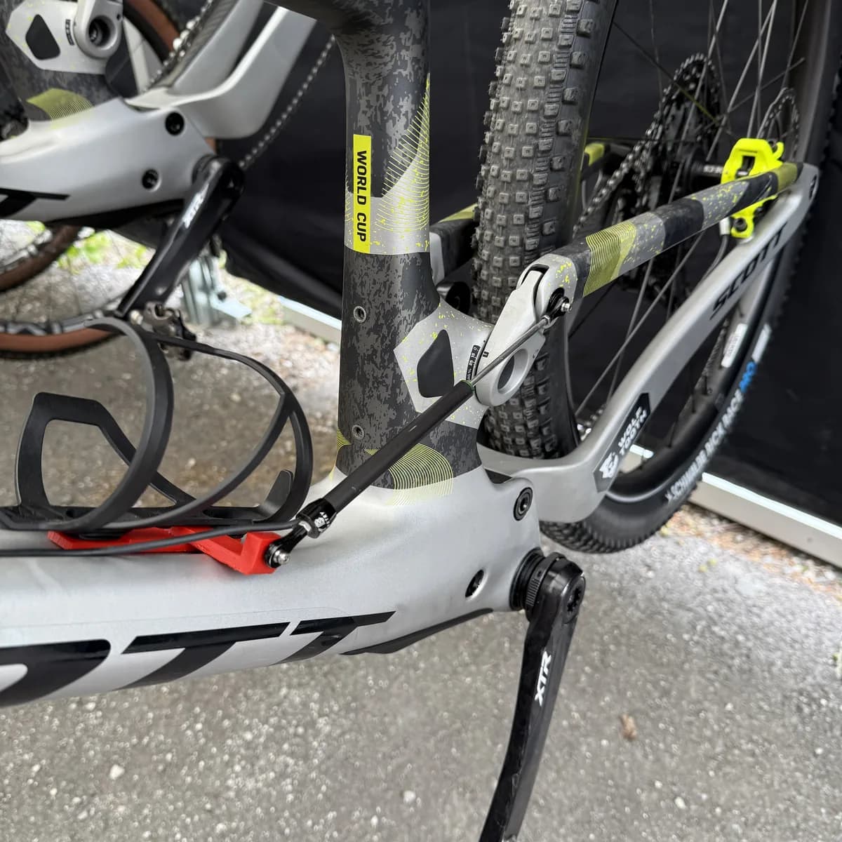 A Scott Spark World Cup outdoors on a stand, with a red printed bracket low on the frame and a linear sensor running up to the rocker. No shock is visible anywhere on the bike.
