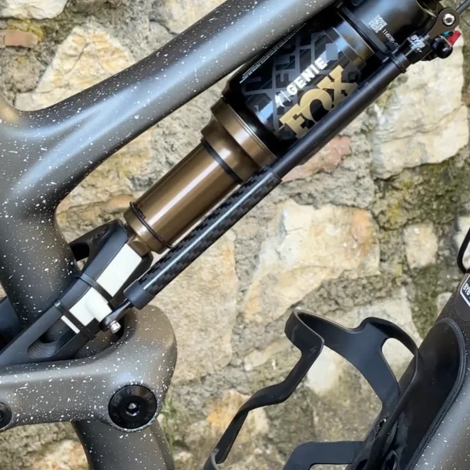 A Specialized Stumpjumper 15 against a stone wall, with the sensor running from a printed bracket at the lower linkage up alongside the Fox Genie rear shock.