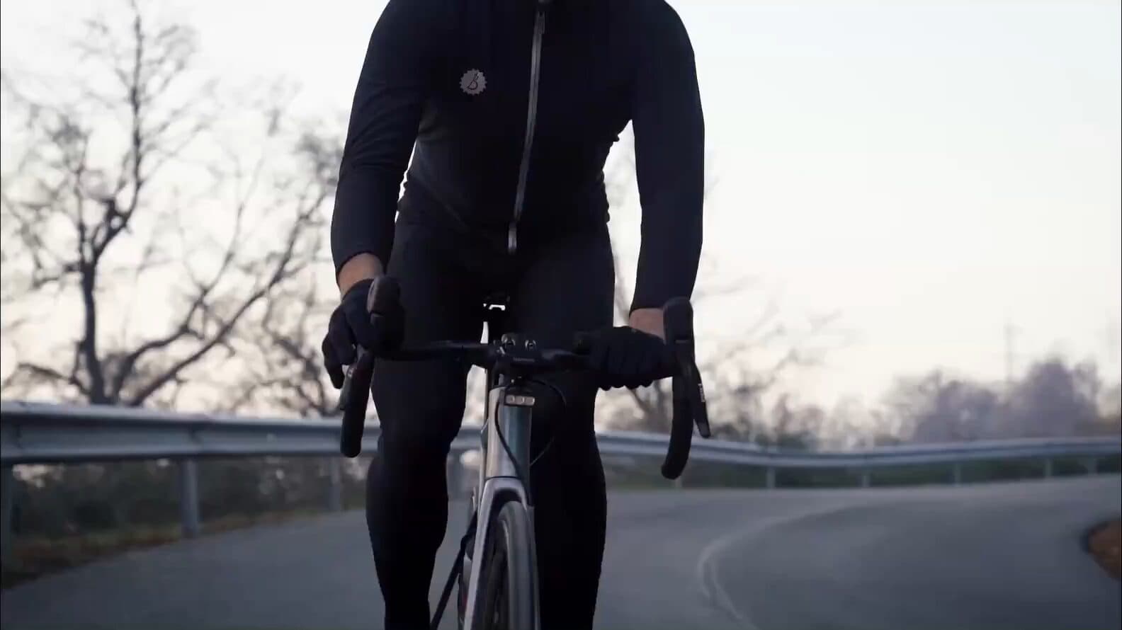A road cyclist riding towards the camera at dusk on an empty road, a BYB Focus mounted beneath the handlebar.