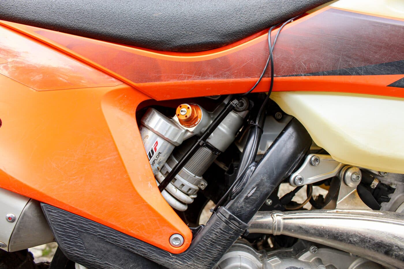 A BYB Telemetry sensor fitted alongside the WP shock of an orange KTM enduro bike, its cable running up under the seat.