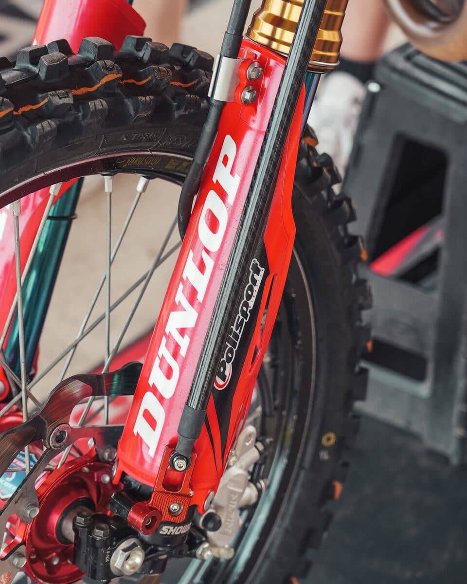 A BYB Telemetry sensor fitted down the leg of a red Showa motocross fork, its upper clamp on the fork guard and its lower bracket at the axle clamp, with the brake disc and Dunlop tyre behind.