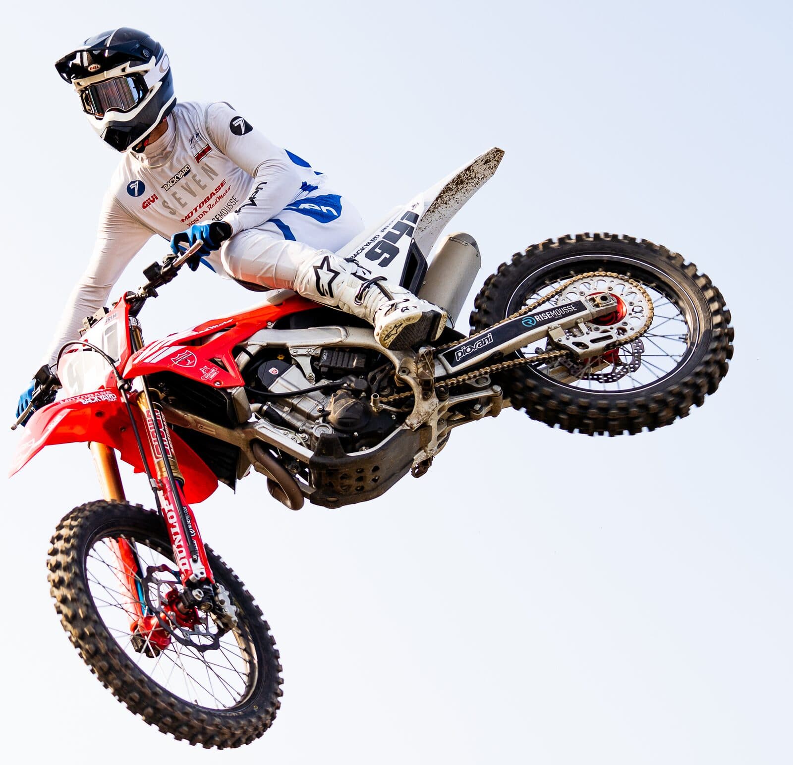 A red Honda motocross bike airborne side-on against a clear sky, with a BYB Telemetry linear sensor running down the fork leg and the acquisition unit mounted on the front number plate.