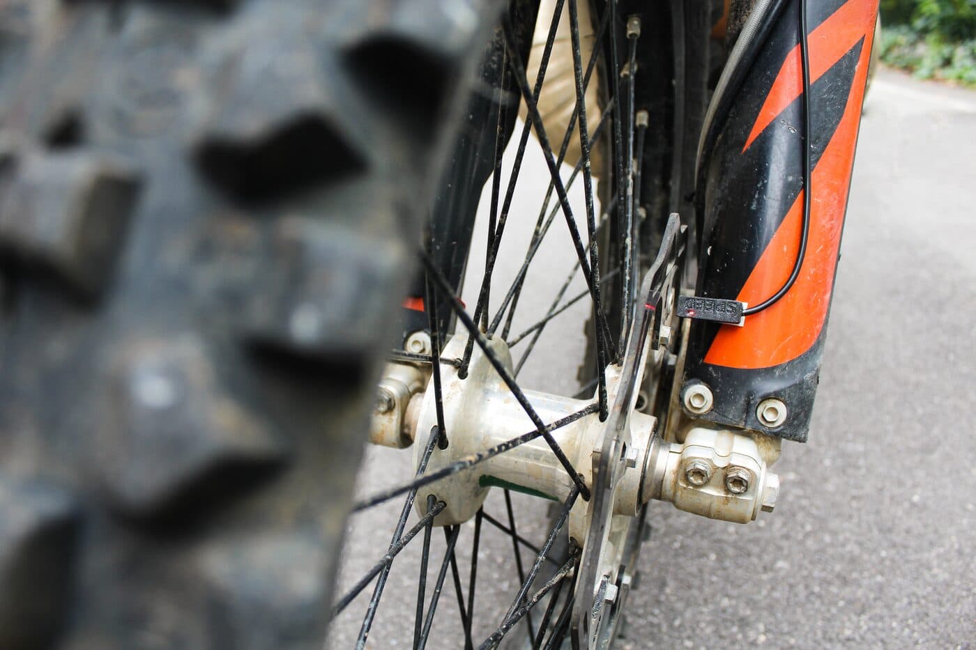 A BYB Telemetry speed sensor marked SPEED, mounted to the fork guard of a KTM on a bracket reaching in toward the front wheel spokes.