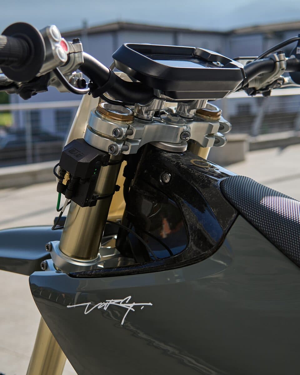 A BYB Telemetry acquisition unit mounted at the triple clamp of a motocross bike, its wiring running down behind the fork leg, with the handlebar and front number plate above it.