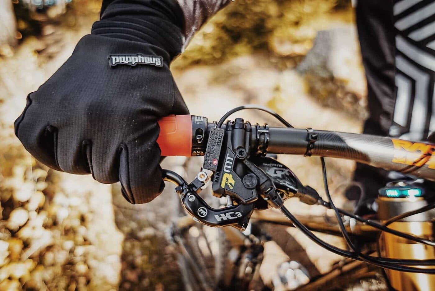 A BYB Telemetry brake sensor fitted at the lever on a mountain bike handlebar, with a gloved hand on the grip and the hydraulic hose unbroken.
