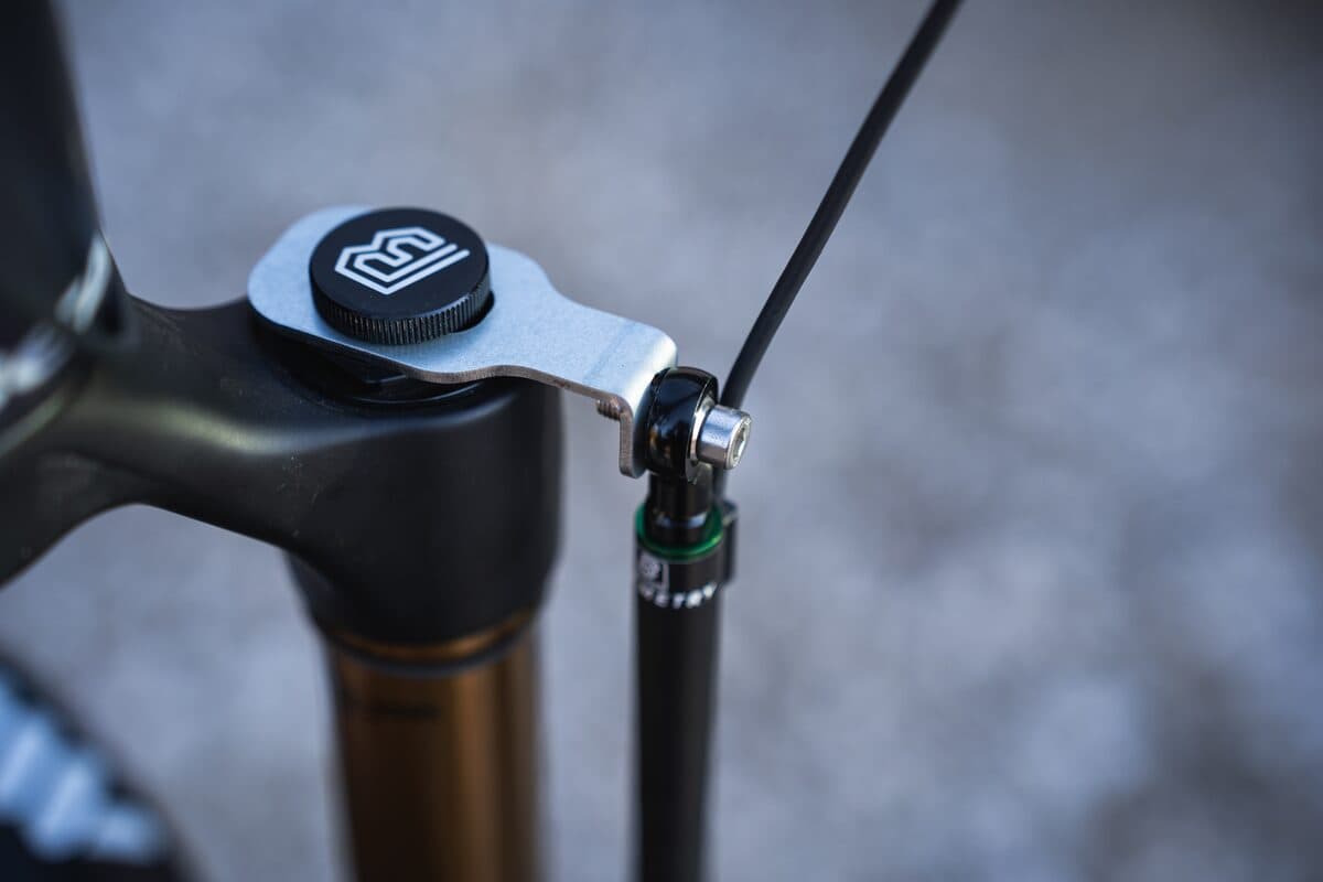 The upper mount of a BYB Telemetry fork sensor on a mountain bike fork crown: an alloy bracket under a BYB-branded cap, with the sensor's ball joint and cable running down beside the stanchion.