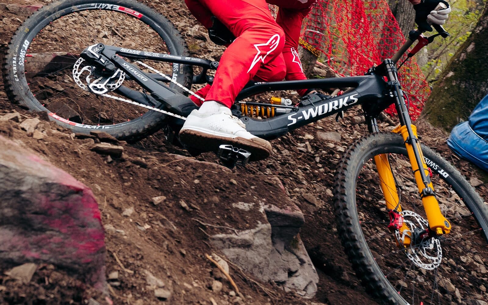 A Specialized S-Works downhill bike ridden through a rocky World Cup practice section, side on, with the BYB Telemetry fork sensor visible down the yellow fork lower, the shock sensor across the coil shock, and the acquisition unit on the down tube.