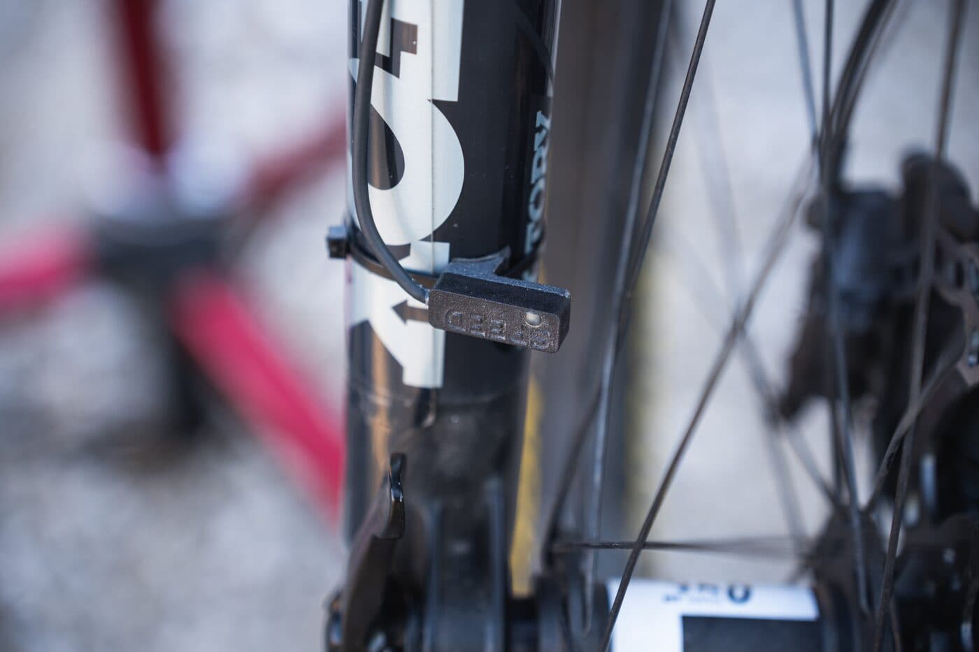 A BYB Telemetry speed sensor embossed SPEED, cable-tied to the fork lower of a mountain bike with its cable running up the leg and the front wheel and disc brake behind it.